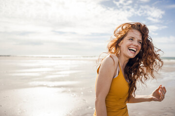 Netherlands, Zeeland, portrait of laughing redheaded woman on the beach