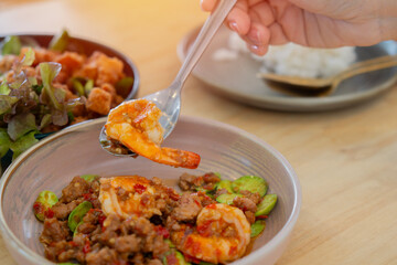 A young woman's hand uses a spoon to scoop up a menu of stir-fried Sator with shrimp