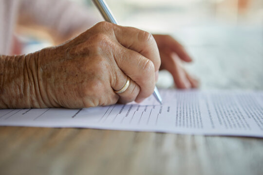 Hands of senior woman filling form at table