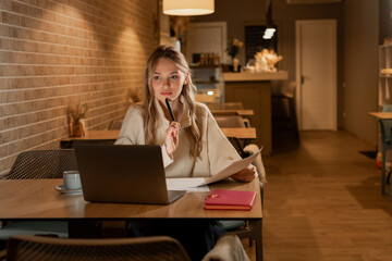 Pensive blonde woman sitting at table work at laptop thinking of problem, thoughtful employee girl...
