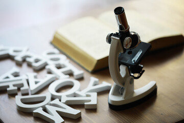 Microscope on Wooden Desk with Open Book and Scattered White Letters