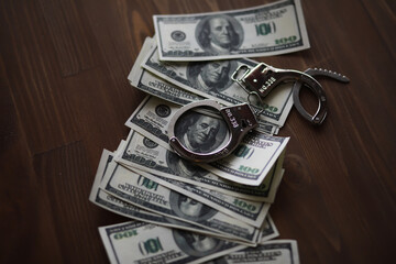 Handcuffs on Pile of Hundred-Dollar Bills on Wooden Table: Concept of Crime and Finances