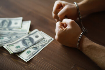 Handcuffed Hands and Money on Table - Concept of Crime, Arrest, and Financial Fraud