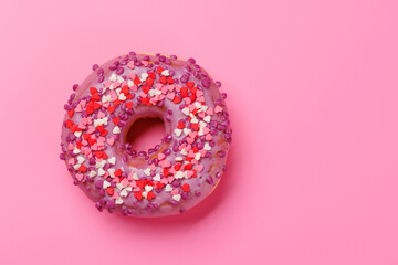 A sweet donut adorned with heart-shaped decor on a pink background