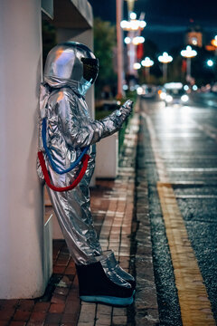 Spaceman standing at a bus stop at night holding cell phone