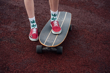 Woman's legs in socks and sneakers standing on carver skateboard