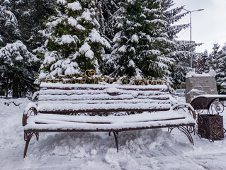 A bench covered in snow next to a bench in a park