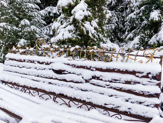A wooden bench covered in snow next to a fence