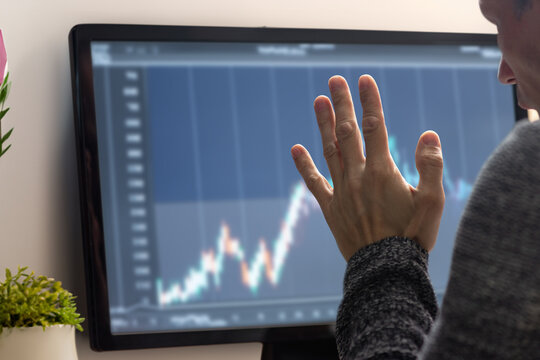 Young man working on computer and monitoring digital trade charts on screen. Home-based beginner trader man, back view, studying stock charts on monitor. Free time business