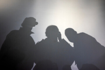 Ombre di tre persone su di un muro bianco illuminato.