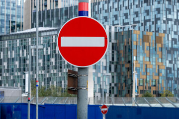 A bold no entry sign stands prominently, framed by a backdrop of striking modern architecture, encapsulating the restrictions and regulations of urban living.