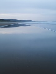 A photo of a tranquil beach at sunrise, with gentle waves washing over smooth, golden sand.
