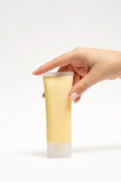 Yellow face mask tube held in cropped hand against white backdrop