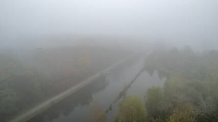 A serene view of a meandering river enveloped in soft autumn fog, evoking a beautiful sense of...