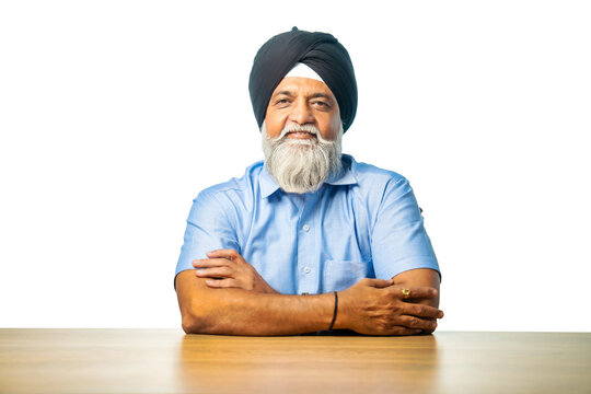 Senior Sikh man sitting at table with white background, expressing various emotions and gestures