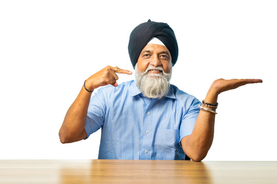 Senior Sikh man sitting at table with white background, expressing various emotions and gestures