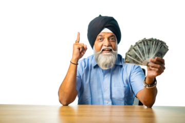 Elderly Sikh man with Indian currency fan, sitting at table, showing happy expression, success sign