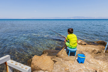 Child Sitting on a Rock Fishing Near Clear Water Shore