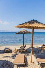 Straw umbrellas and wooden sunbeds scattered on a sandy beach overlooking the serene blue sea.