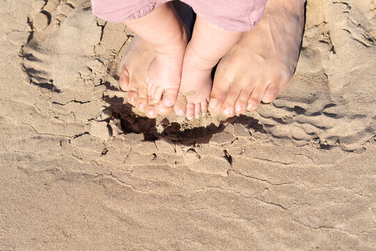 Mom and daughter feet on the beach on sand. close up top view baby and father feet. first steps child. Summer beach background. vacation