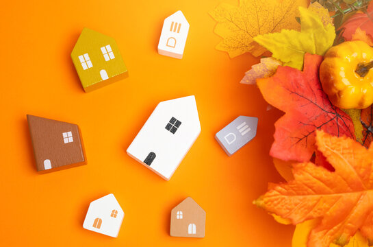 Miniature houses and autumn leaves on orange background. Autumn and real estate concept. Decor and decorations. Flat lay