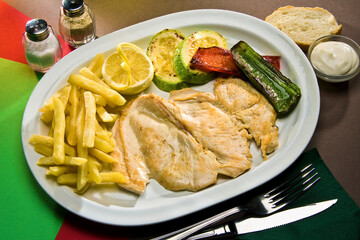 Plato de pechuga de pollo asada con verduras asadas, papas fritas y limón.