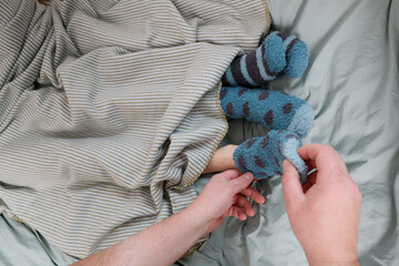A father's hand removes warm socks from the feet of children in bed