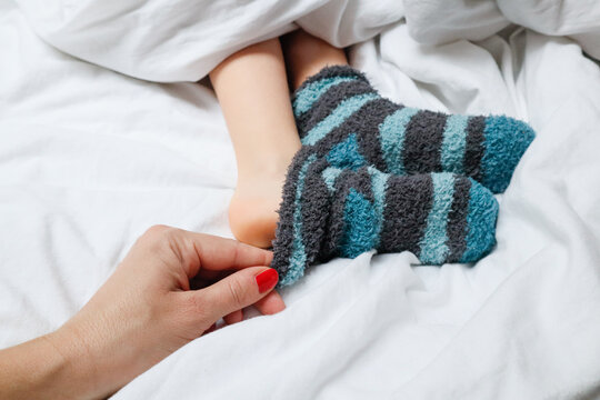 Mom pulling off baby&rsquo;s sock while child lies in bed
