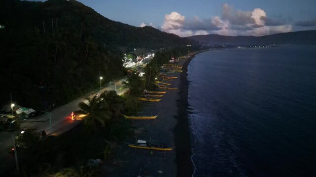 Picturesque aerial dolly of tropical island coastline lined with local fisherman boats and lush hillside at Bato, Catanduanes during the evening.
