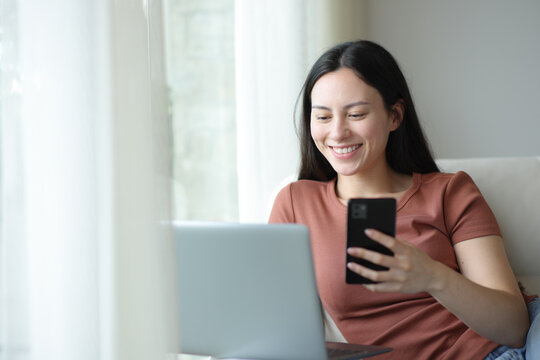 Happy asian woman using multiple devices sitting in a sofa