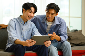 Happy young gay male couple using digital tablet on sofa. LGBT, love and lifestyle relationship concept