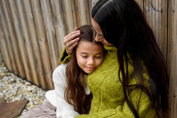 Portrait of beautiful mother with young daughter, sitting together and embracing.