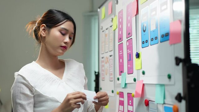 Attractive female designer points to whiteboard with project of website phone ux ui and explains design process during presentation Online planning in the modern office.