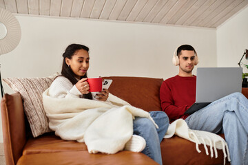 A couple shares warmth on a sofa, using gadgets in a chic winter setting.