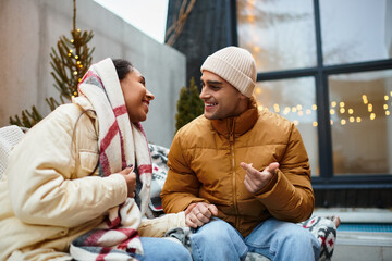 Obraz premium Two people share a warm moment outdoors, wrapped in winter attire near festive lights.