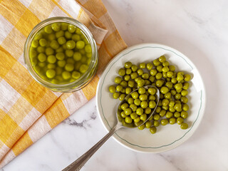 Marinated organic peas on a plate over marble countertop. Canned green peas on a white dish and...