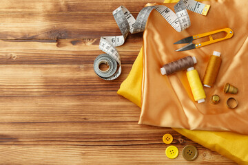 Crafting essentials arranged on golden satin fabric with sewing tools and colorful buttons scattered around