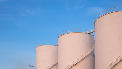 Three storage fuel tanks in petrochemical refinery area with orange sunlight on surface against blue evening sky background, low angle view with copy space