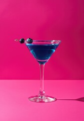 Blue cocktail in martini glass with blueberries against vibrant pink background