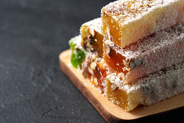 Colorful traditional sweets stacked on a wooden board with coconut flakes