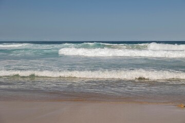 Ocean waves on sandy beach under blue sky