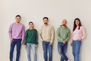 Fototapeta premium Portrait of a group of young confident smiling friends students or colleagues in casual clothes standing together on a row isolated on a white background and looking positively at camera.