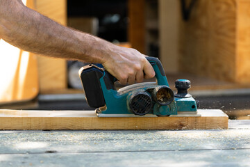 Carpenter using electric planer smoothing wooden plank in workshop