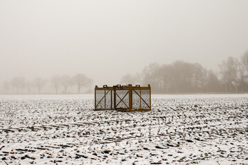 Iron crate for harvest stands on meadow with snow, huge void