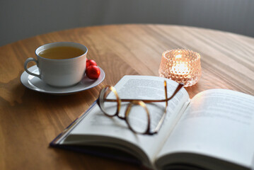 Open book with glasses, a cup of tea and a candle