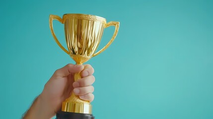 A close-up of a hand holding a shiny gold trophy against a turquoise background, symbolizing achievement and success.