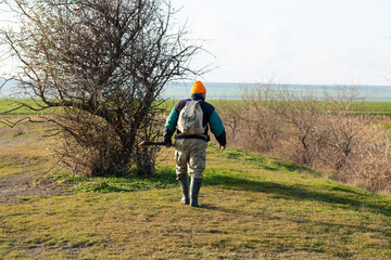 Mature hunter man holding a shotgun and walking through a field