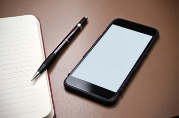Modern workspace with smartphone, notebook, and pen on wooden desk during day