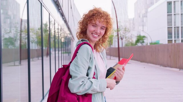 Cheerful red-haired student holding a red folder in a bright outdoor setting