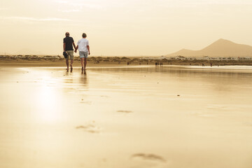 Back view of active senior couple walking on a beach in the golden sunset in Canary Islands
